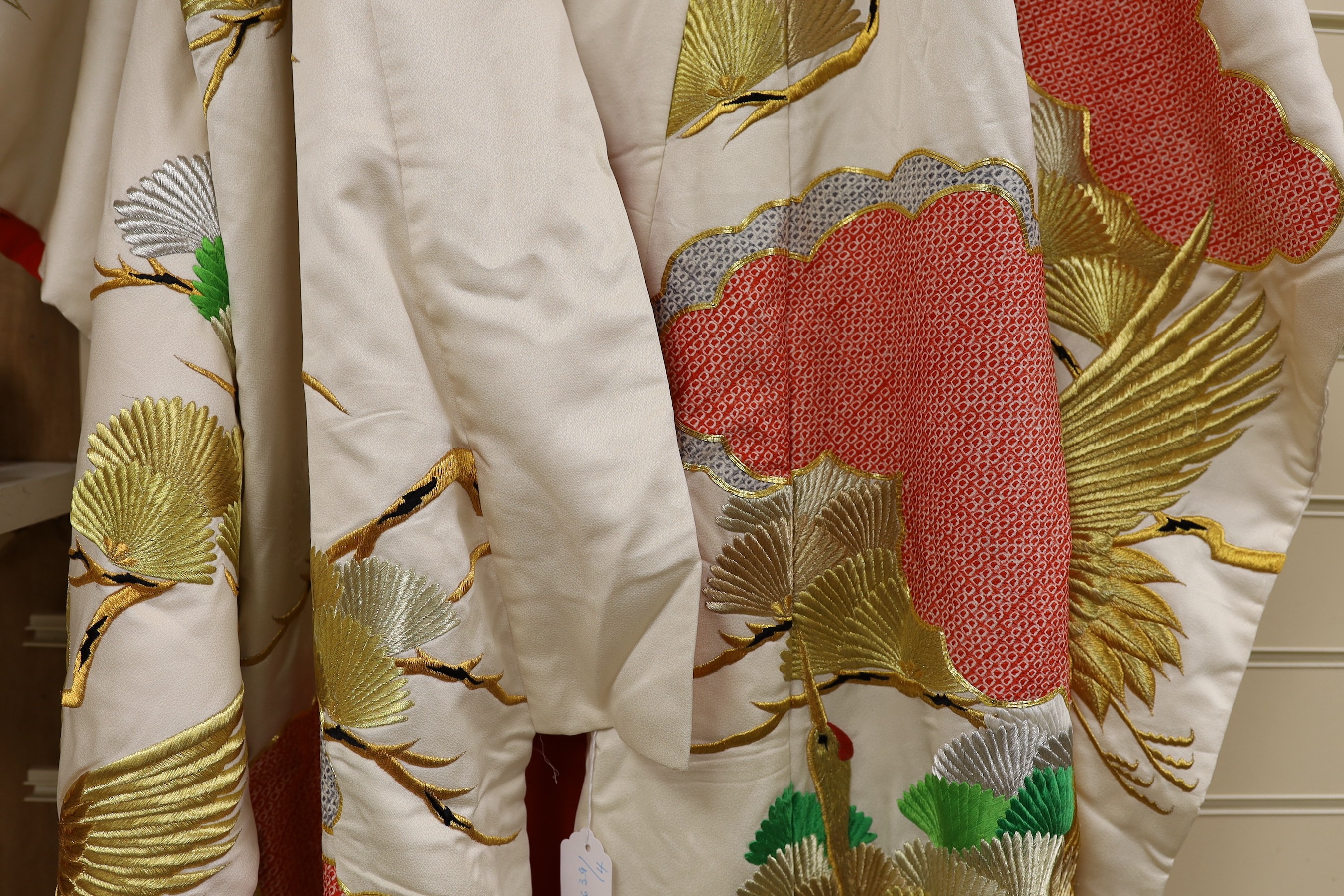 A Japanese cream ground ceremonial kimono, embroidered with coloured silks and metallic embroidery, in an all over design, with flame red silk lining